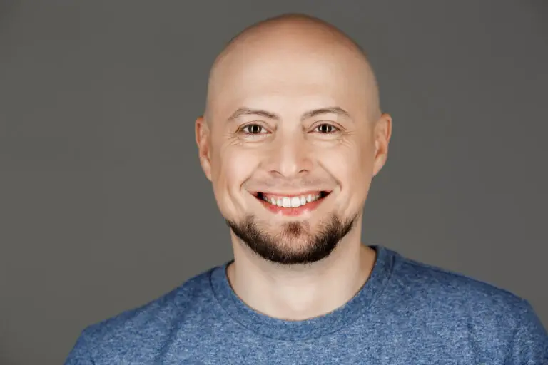 Close up portrait of handsome middle-aged man in grey shirt smiling at camera over dark background